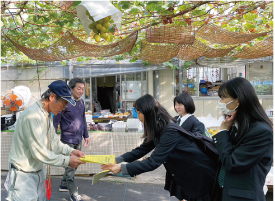 世代間交流イベントのチラシを男性に渡している女子生徒３人の写真