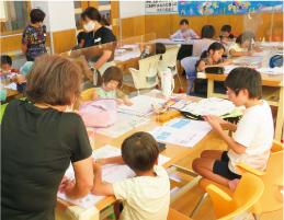 「みんなで宿題！3days～ハッピー夏休み♪～」で宿題をしている子どもたちと、それを見守る第2部会の皆さんの写真