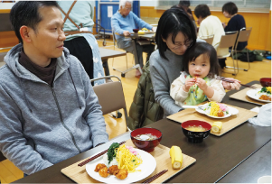 男性と女性、女性の膝に座る子どもの3人で食事をしている写真
