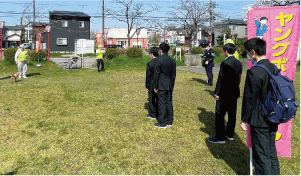 白根高校の生徒が「わんわんパトロール」の出発式でヤングボランティアののぼり旗を持ち、話を聞いている写真
