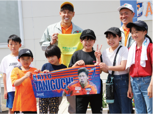 谷口海斗選手、小見洋太選手と谷口選手のタオルを広げて持つ子どもたちの集合写真