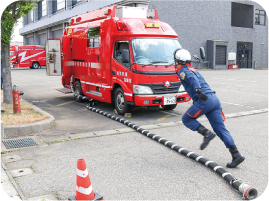 ホースを一直線に伸ばし、駆け足で作業に戻る紺色のユニホームにヘルメットを着用した隊員の写真