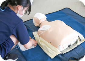 女子中学生が練習用のマネキンの胸部にパッドを装着している写真