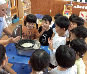 子どもたちが炊き立てのご飯が入ったジャーをのぞき込む写真